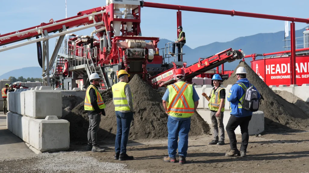 Five people in hi-vis vests talk in front of a sand pile and the Tyrone mobile wash plant, while another person watches from a platform above.