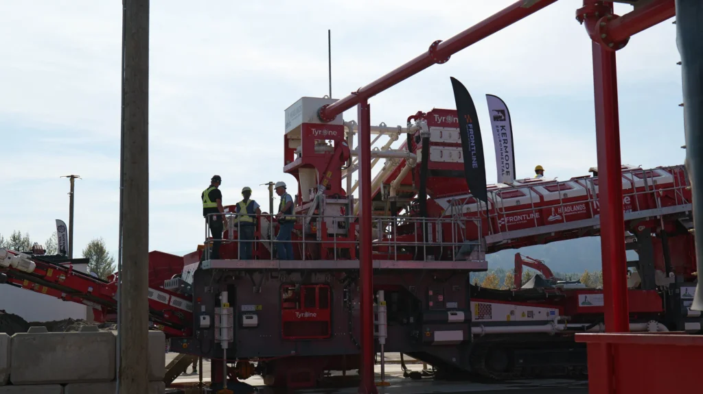 Three people stand in silhouette on the upper platform of a Tyrone TrackWash Pro.