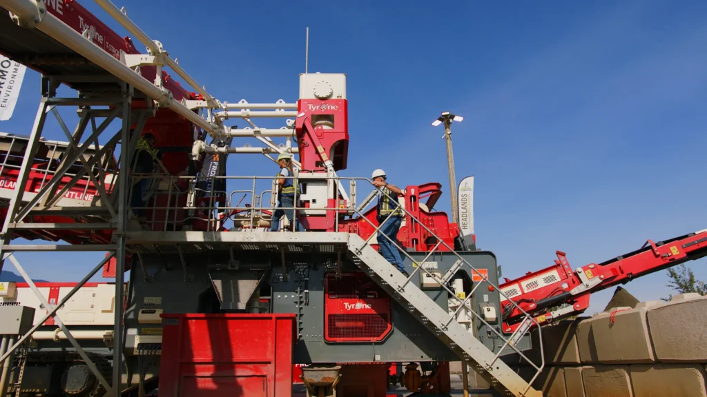 Two people in hard hats climb a galvanized staircase on the red Tyrone wash plant against a deep blue sky.